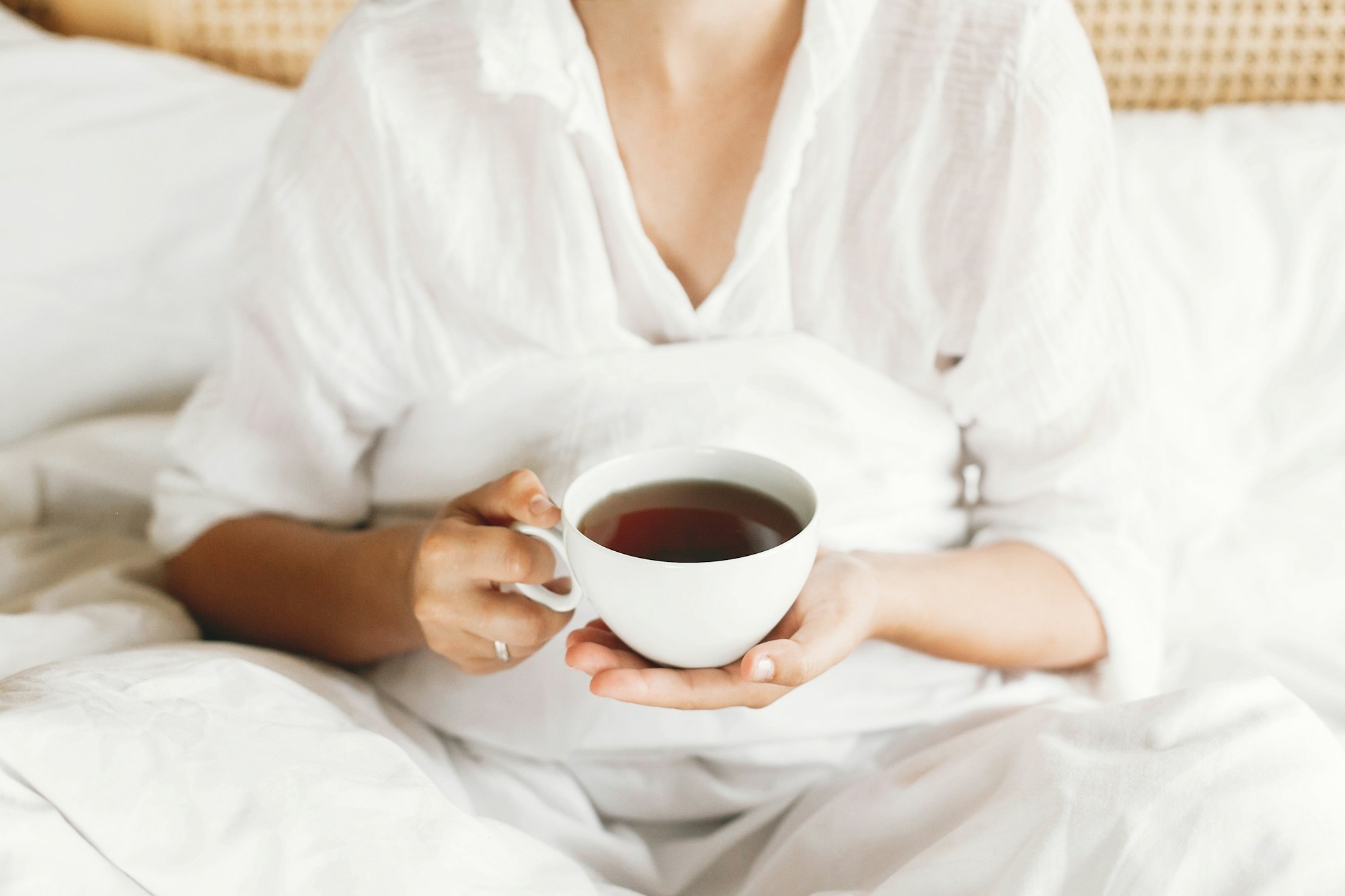 Beautiful happy young woman drinking tea in bed