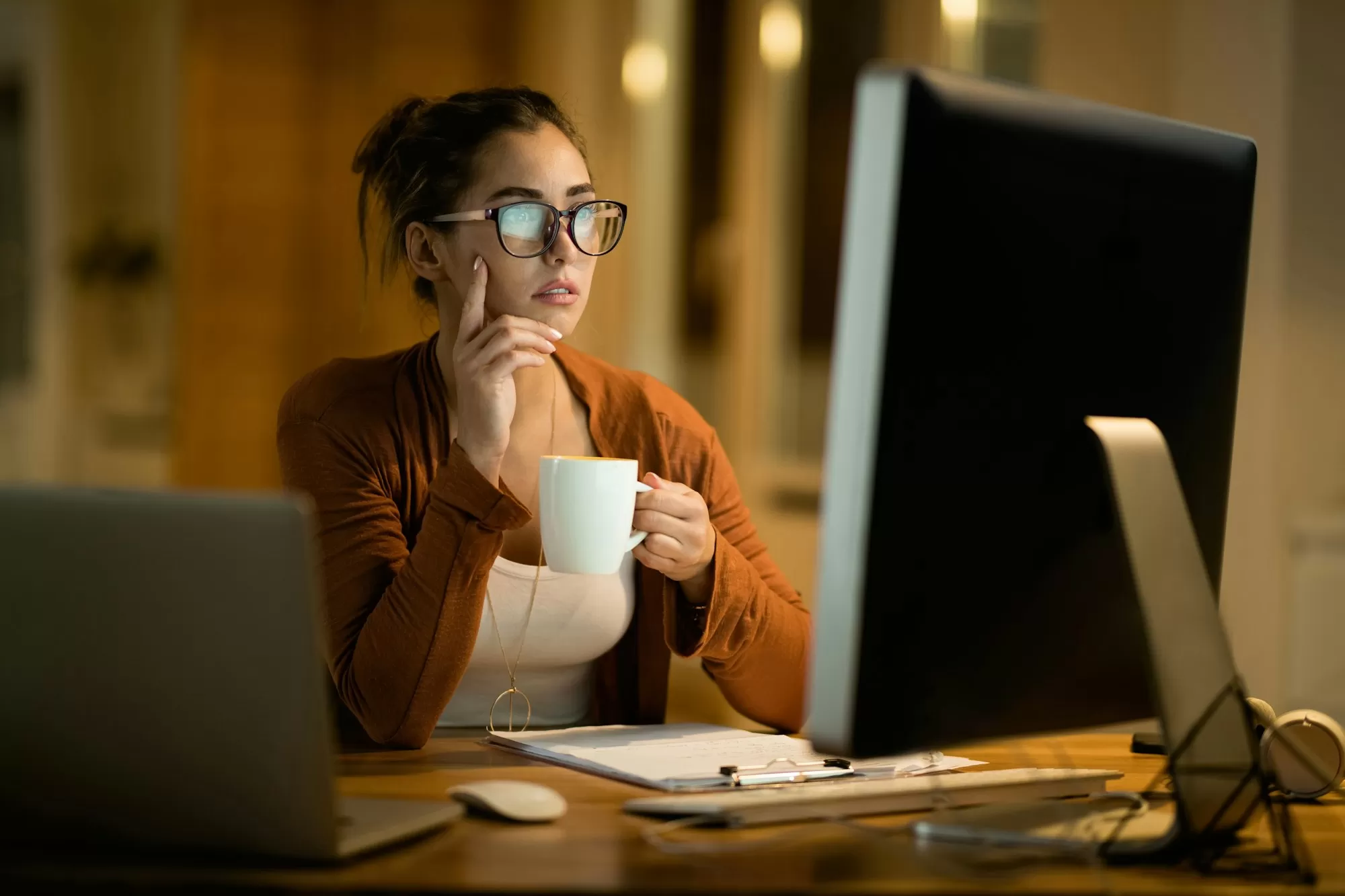 Young pensive woman drinking tea while reading e-mail on computer at home.